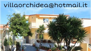 Eine Villa mit gelber Fassade, einer Treppe, die zu einem Balkon führt, und Kübelpflanzen.