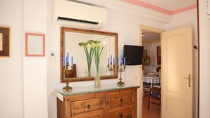 A room with a wooden dresser, a mirror, a vase with flowers, and a television in the background. - Coronado 129 Apartment by Casasol (Nerja)