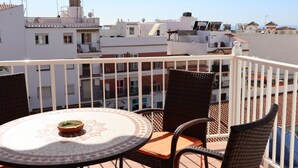 A balcony with wicker chairs and a table, overlooking a cityscape with buildings and a clear sky. - Coronado 129 Apartment by Casasol (Nerja)