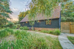 A rustic wooden house with a sloped roof, surrounded by a well-maintained garden and a stone pathway leading to the entrance. - Stansted Airport - Beautiful Annexe with Parking (Takeley)