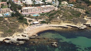 Vue aérienne d’une station balnéaire comprenant plusieurs bâtiments, une plage et une baie rocheuse.