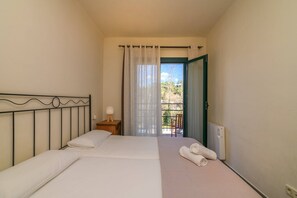 A bedroom with a bed, a nightstand, a window with curtains, a radiator, and a door leading to an outdoor area.