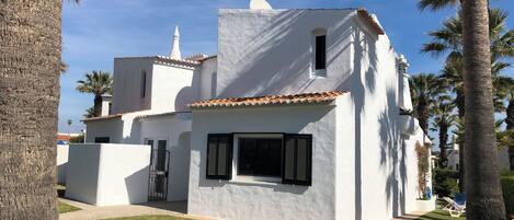 A white building with a tiled roof, surrounded by palm trees and a well-maintained lawn.