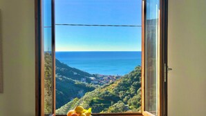 A window with a view of a coastal landscape, a plate with fruit, and a wooden frame.