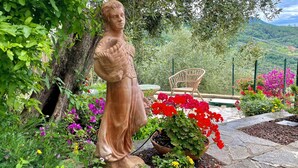 A garden with a statue, a wicker chair, and a variety of colorful flowers.