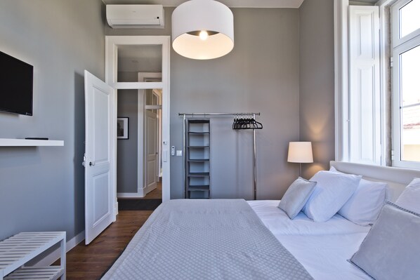 A bedroom with a bed, a wardrobe, a hanging clothes rack, a bedside lamp, and a television on the wall.