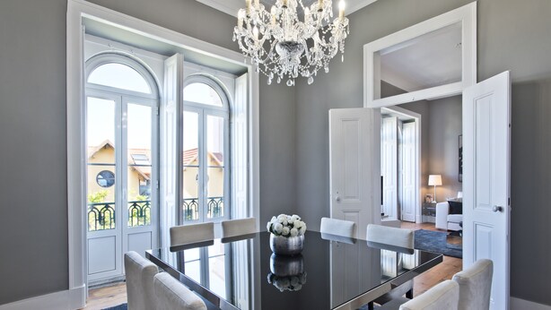 A dining area with a glass table, white chairs, and a chandelier. - An apartment with an amazing terrace (Estoril)
