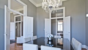 A dining room with a glass table, white chairs, and a chandelier. - An apartment with an amazing terrace (Estoril)
