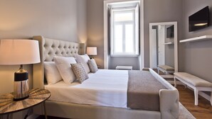A modern bedroom with a large bed, bedside lamps, a bench, a TV, and a window with natural light. - An apartment with an amazing terrace (Estoril)