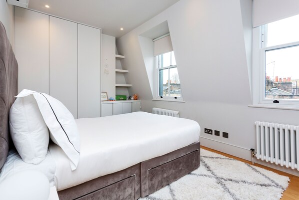 A modern bedroom with a bed, built-in wardrobe, and a window with a view of buildings. - Wood Quirk, by Veeve (London)