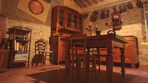 A rustic kitchen with wooden cabinets, a wooden dining table, and chairs. There is a bookshelf with books and a clock on the wall. - FANTASTIC RURAL HOUSE IN FULL RELAXATION IN THE HILLS WITH SWIMMING POOL (CIVITELLA DI ROMAGNA)