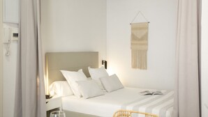 A neatly made bed with white linens and pillows, a bedside table with a lamp, and a wall-mounted macrame piece.