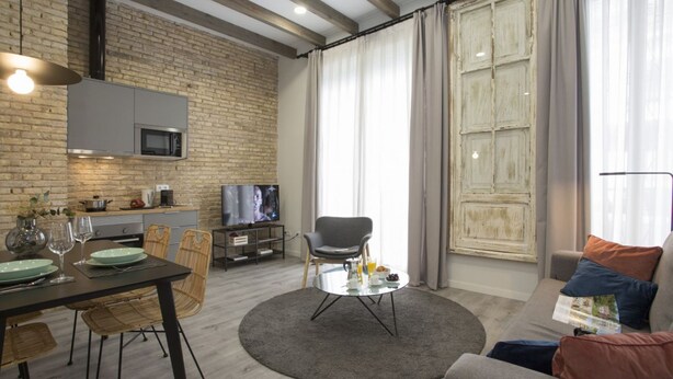 A modern living room with a dining area, a kitchen, and a large window with curtains.