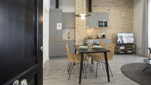 A modern kitchen with a brick wall, a dining area with a table and chairs, and a television in the background.