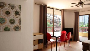 Un espace repas comprenant une table et des chaises, un ventilateur de plafond et une vue sur les bâtiments à travers de grandes fenêtres.