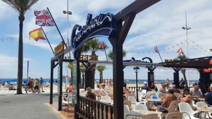 Un restaurant situé en bord de mer, avec une terrasse, des palmiers et des drapeaux.