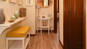 Un pasillo con piso de madera, un banco, una pequeña mesa con lámpara, un espejo y cuadros en la pared.