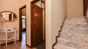 Una escalera con escalones de mármol, una puerta de madera, un espejo y una mesita con una lámpara y jarrones.