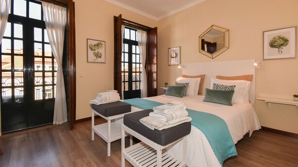 Un dormitorio ordenado con cama, mesitas de noche y una ventana con cortinas.