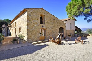 A stone building with a wooden door and windows, a gravel driveway, and a view of the countryside. - Beautiful apartment for 4 guests with A/C, pool, WIFI and TV, close to San Gimignano (Poggibonsi)