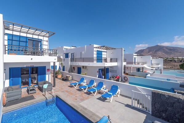 A poolside area with lounge chairs, a pool, and a building with blue shutters.
