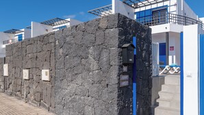 Un mur de pierre avec une porte bleue, un bâtiment blanc avec des volets bleus et un ciel d’un bleu éclatant.