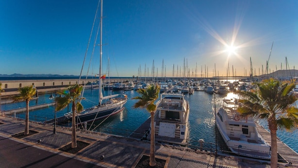 Un port de plaisance où sont amarrés de nombreux bateaux, un ciel dégagé et le soleil qui se couche à l’horizon.