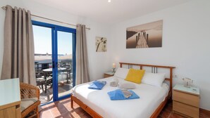 Une chambre d’hôtel avec un lit, un bureau, une chaise, un balcon avec des tables et une vue sur la mer.