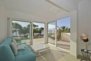 Ein modernes Wohnzimmer mit einem türkisfarbenen Sofa, einem weißen Couchtisch und einer Stehlampe. Große Glasüren führen zu einer Außenpatio mit Blick auf Palmen und einen Pool.