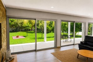 A modern living room with a large sliding glass door leading to a backyard with a lawn and patio furniture. - Casa da Tapada_Grupo Casas Vale do Lima (Ponte de Lima)