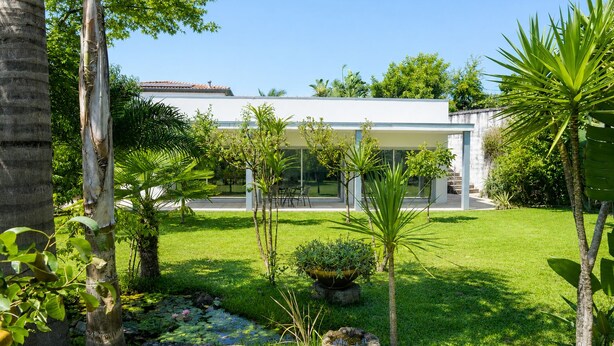 Een modern huis met een verzorgde tuin, inclusief een vijver met waterlelies en diverse planten.