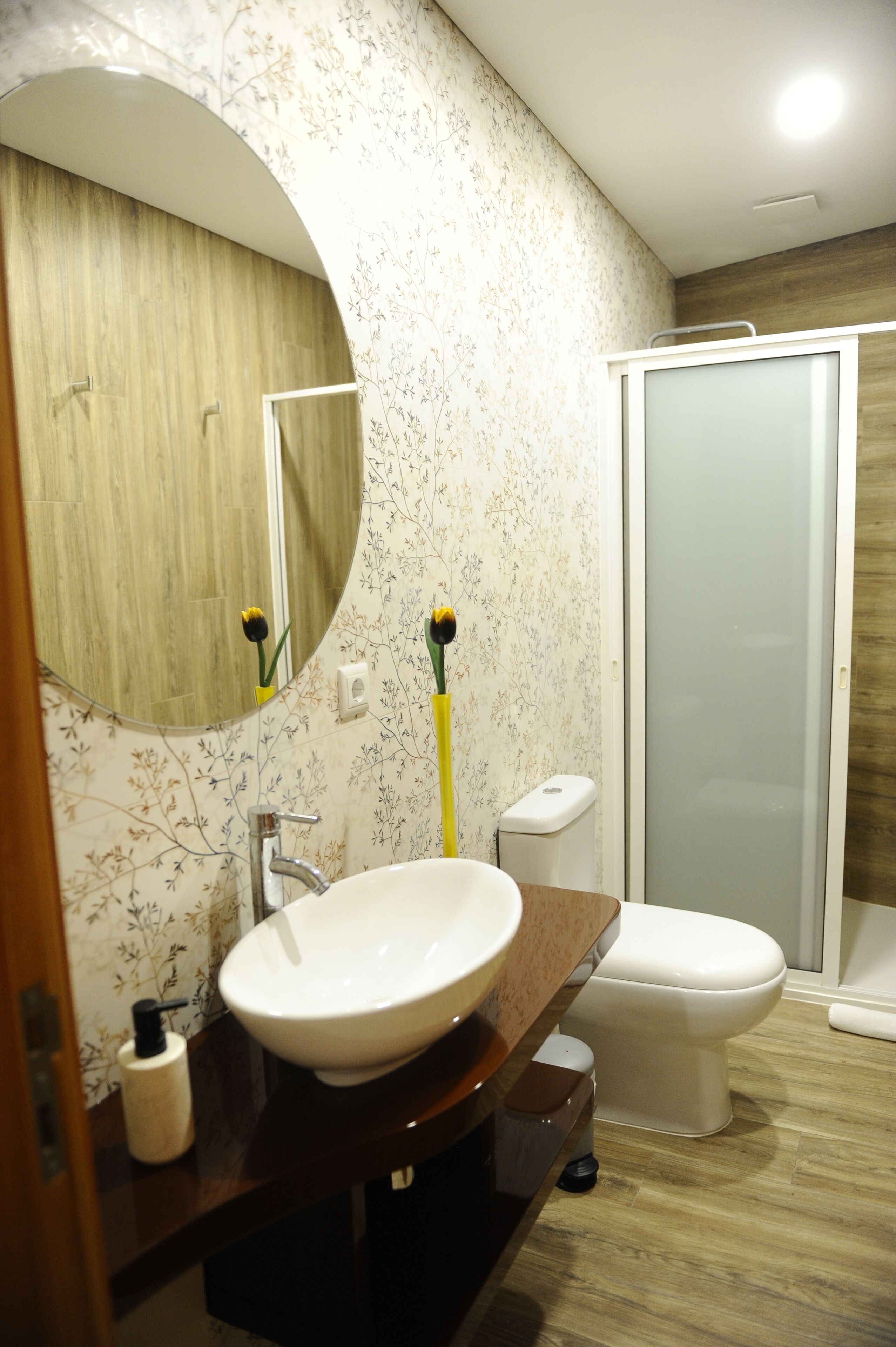 A bathroom with a round mirror, a sink, a toilet, and a shower.