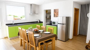 Een moderne keuken met groene kastjes, een roestvrijstalen koelkast, en een eethoek met houten stoelen en een tafel voor vier personen.