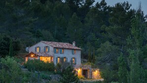 Una casa de piedra rústica con varias ventanas y una chimenea, rodeada de un bosque denso.