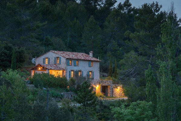 A rustic stone house with multiple windows and a chimney, surrounded by dense forest. - 19th Century Provencal Bastide and Infinity pool (Cotignac)