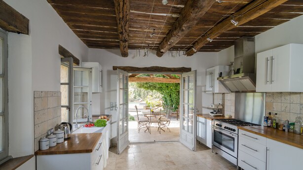 Cocina con armarios blancos, encimera de madera y vistas a un patio exterior con mesa y sillas.