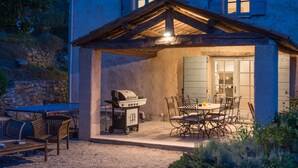 Un patio exterior techado con una parrilla, mesa y sillas para comer.
