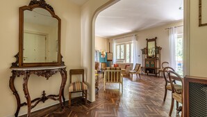 Ein geräumiges Zimmer mit Fischgrätparkett, einem großen, verzierten Spiegel und Blick auf einen Essbereich mit Stühlen und einem Tisch.