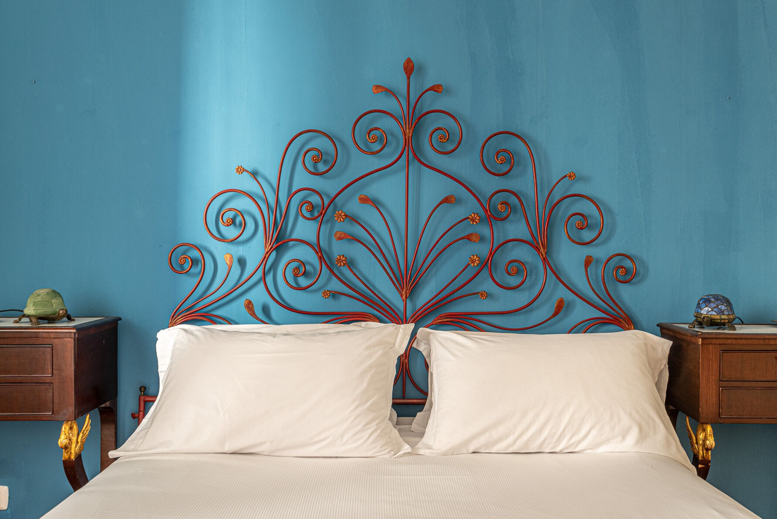 A bed with a decorative metal headboard against a blue wall.