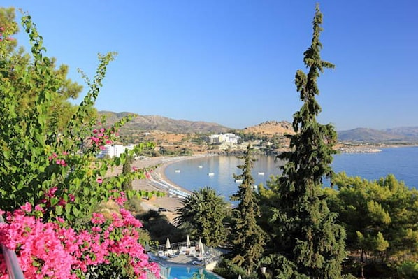 A coastal view with a beach, clear sky, and a pool area with umbrellas.