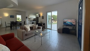 Een ruime woonkamer met een bank, een rode fauteuil, een glazen salontafel en een televisie.