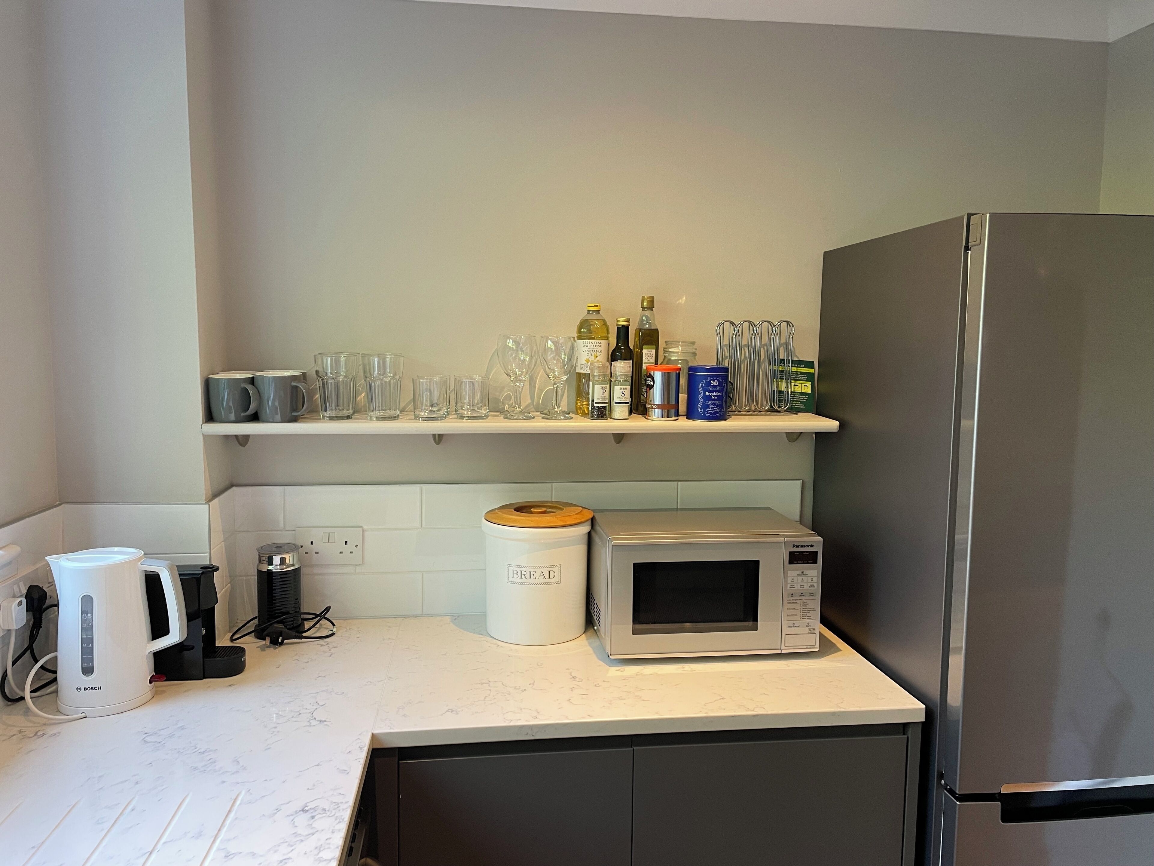 A kitchen with a Bosch coffee maker, a Panasonic microwave, and a stainless steel refrigerator.