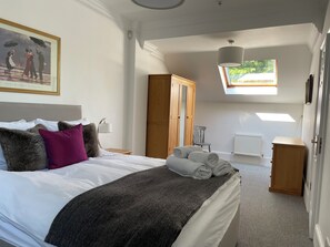 A bedroom with a large bed, a skylight, a painting, and a radiator.
