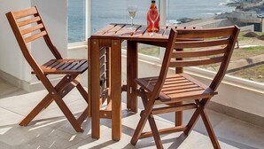 A balcony with a wooden table and chairs, a bottle of wine, and a glass, overlooking a coastal view.