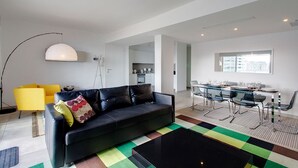 A modern living room with a black sofa, yellow armchair, and a dining area with a glass table and chairs.