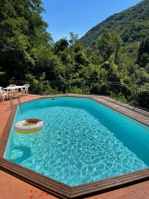 Une piscine rectangulaire à l’eau d’un bleu limpide, entourée d’une terrasse en bois et d’une clôture en métal.