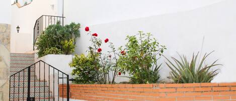 A staircase with a patterned railing, a brick wall, and red flowers.