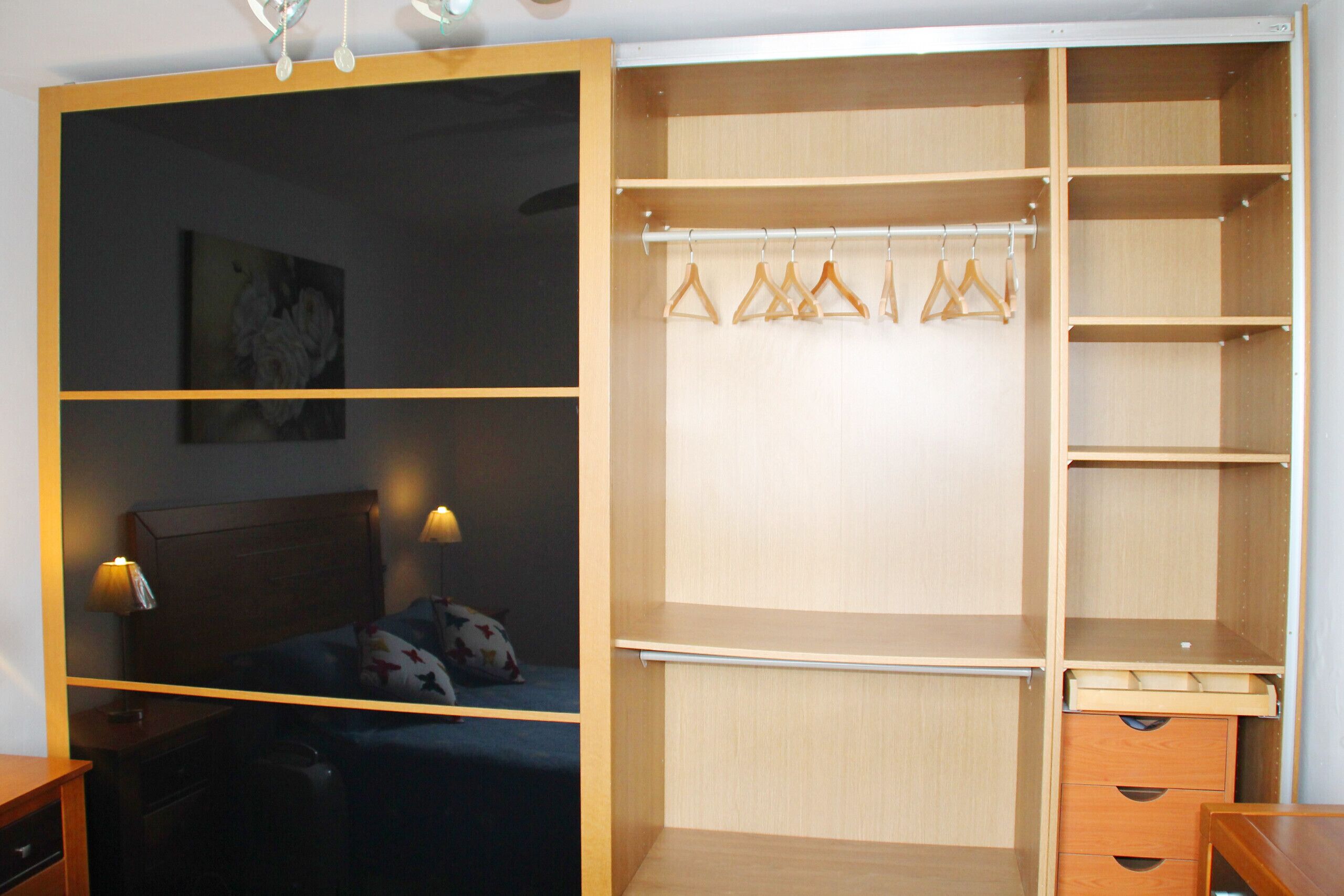 Un dormitorio con cama, mesitas de noche, un armario con puertas abiertas y un closet.