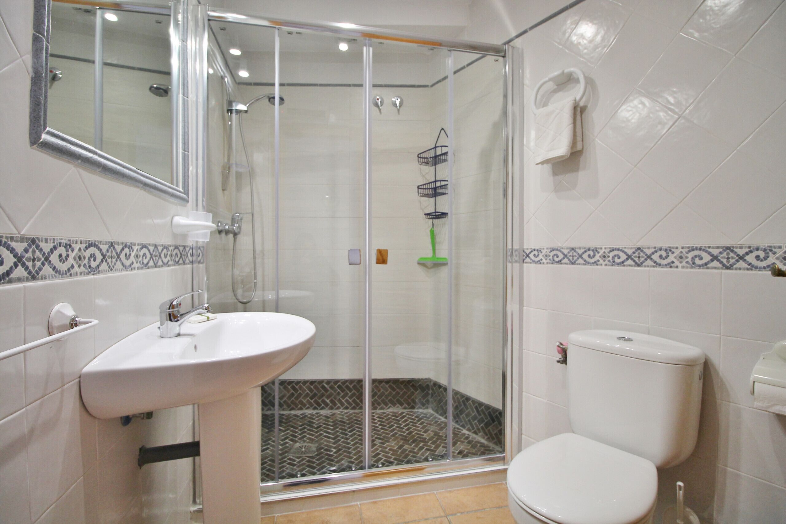 A bathroom with a glass shower enclosure, a white sink, and a toilet.