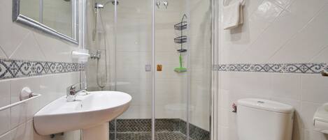 A bathroom with a glass shower enclosure, a white sink, and a toilet.